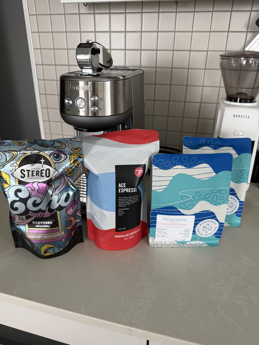 Several coffee bags lined up beside an espresso grinder